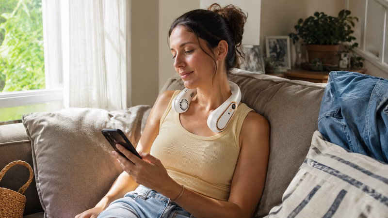 Smiling woman wearing a white neck fan while working at her desk.